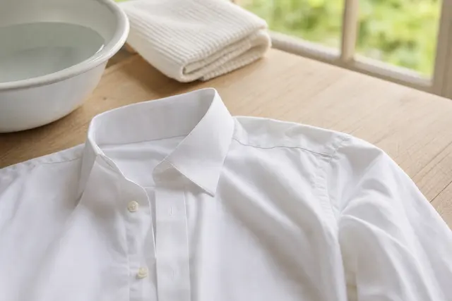 Chemise blanche posée à plat sur une table, col et emmanchure visibles, dans une lumière naturelle de buanderie