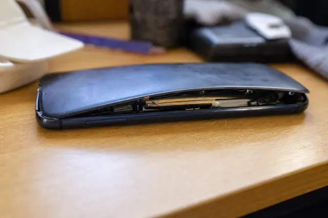 Smartphone posé sur une table avec le dos légèrement bombé, coque entrouverte laissant apparaître la batterie