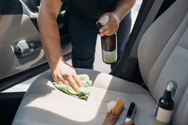 Personne nettoyant l'intérieur d'une voiture d'occasion avec un chiffon microfibre et des produits de nettoyage
