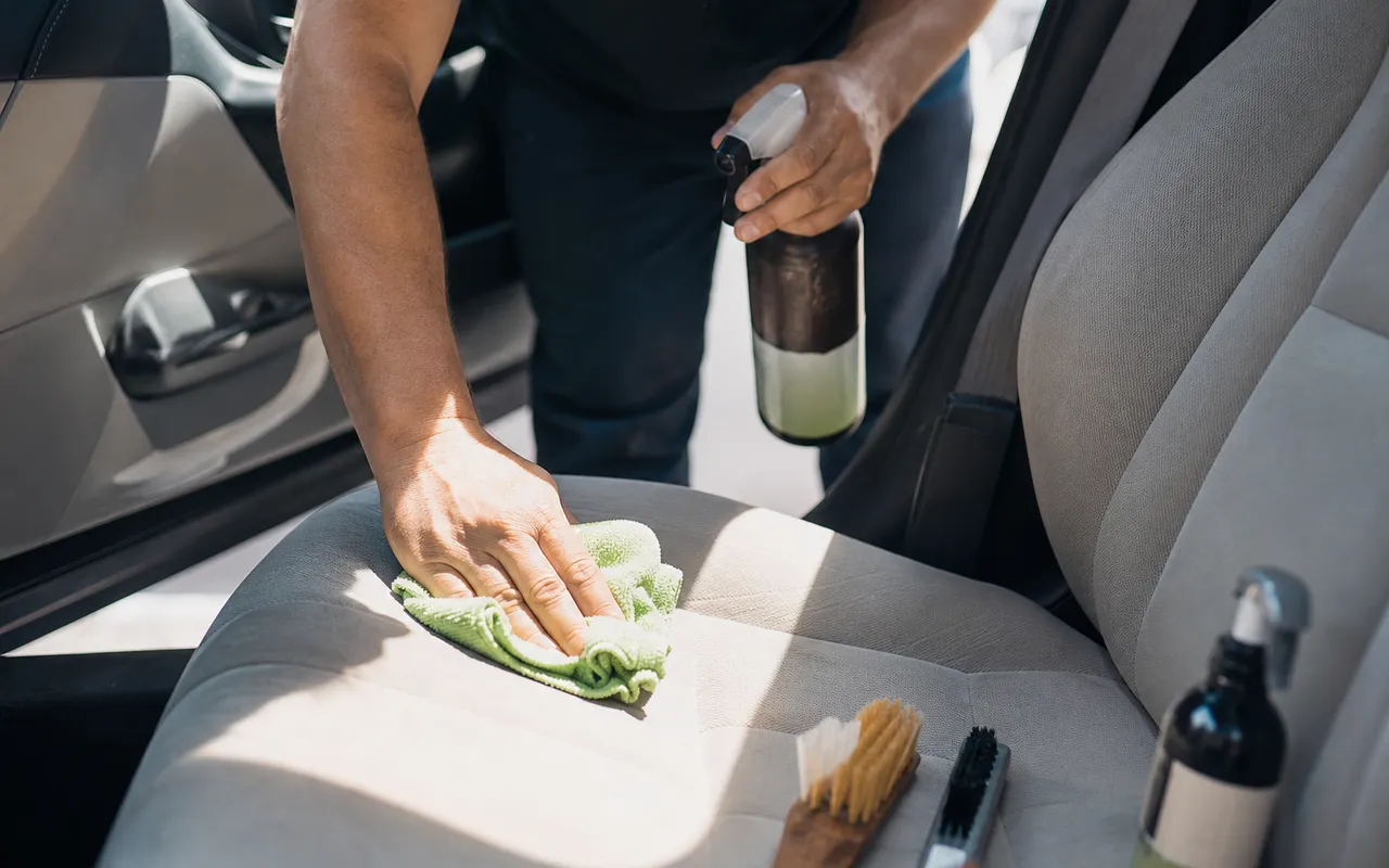 Personne nettoyant l'intérieur d'une voiture d'occasion avec un chiffon microfibre et des produits de nettoyage