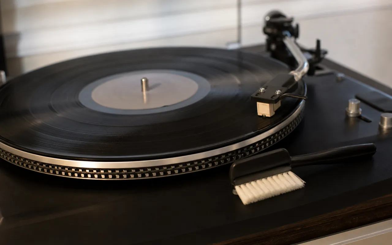 Disque vinyle noir posé sur une platine, brosse anti-statique à proximité