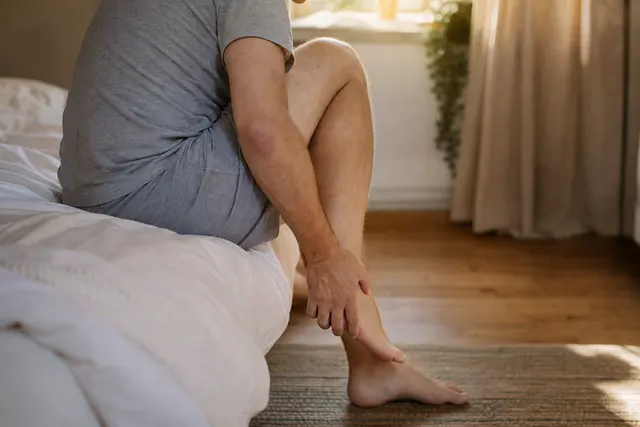 Personne assise au bord du lit le matin, se tenant le talon et la voûte plantaire d'une main