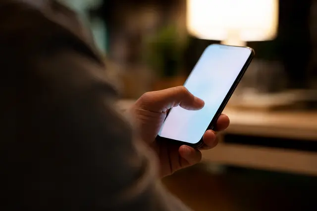 Main tenant un smartphone dont l'écran affiche un scintillement lumineux, gros plan en intérieur