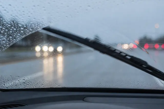 Essuie-glace en action sur un pare-brise sous la pluie, gouttes d'eau et légère traînée visibles sur le verre