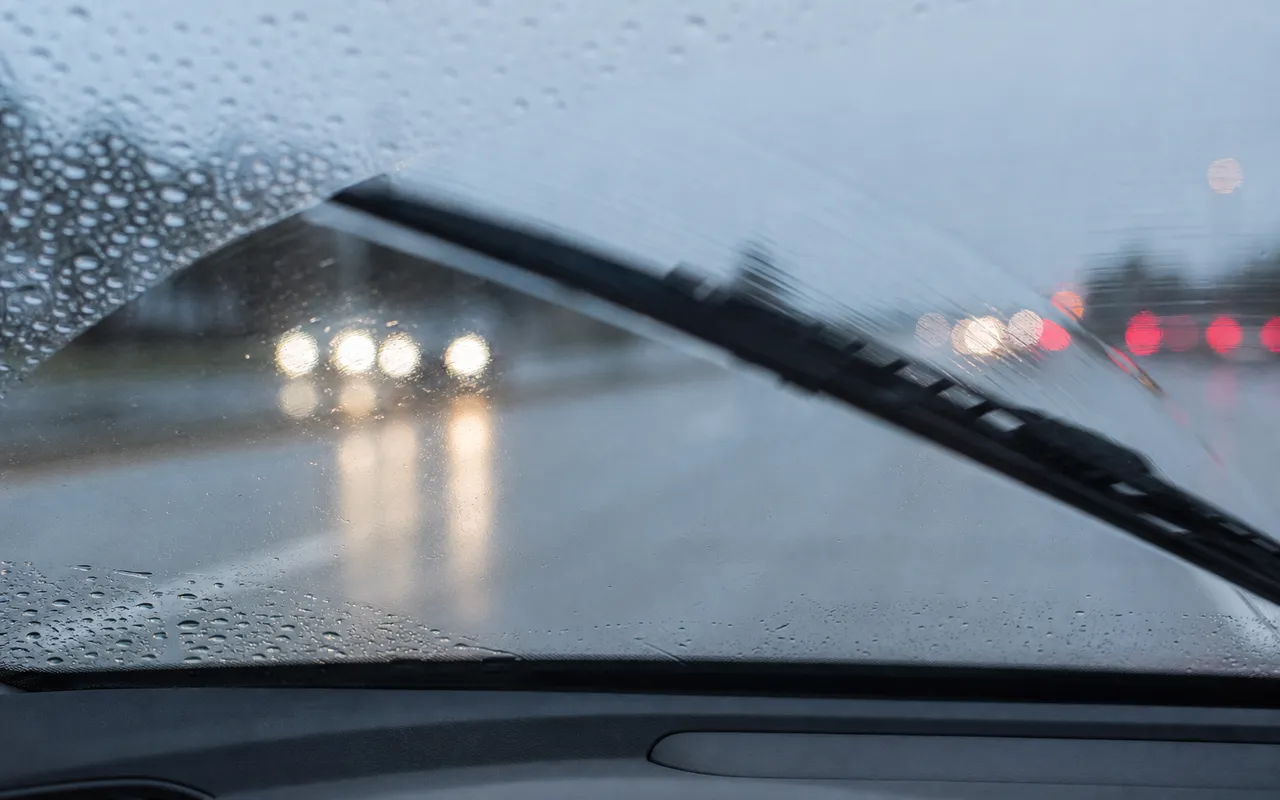 Essuie-glace en action sur un pare-brise sous la pluie, gouttes d'eau et légère traînée visibles sur le verre