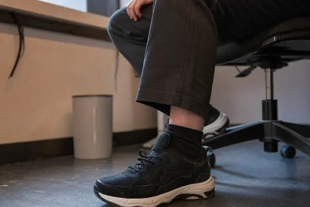Personne assise sur une chaise, main posée près du pied, position de bureau