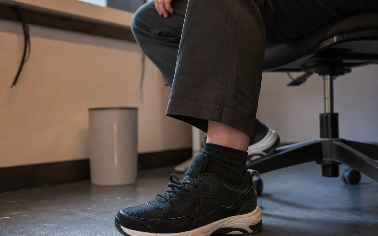 Personne assise sur une chaise, main posée près du pied, position de bureau