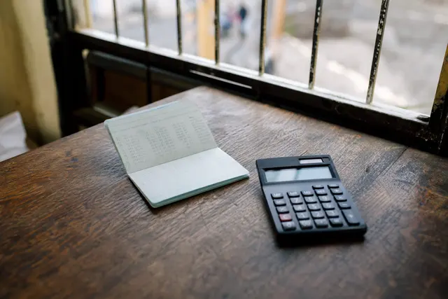 Carnet d'épargne et calculatrice posés sur une table en bois, lumière naturelle douce