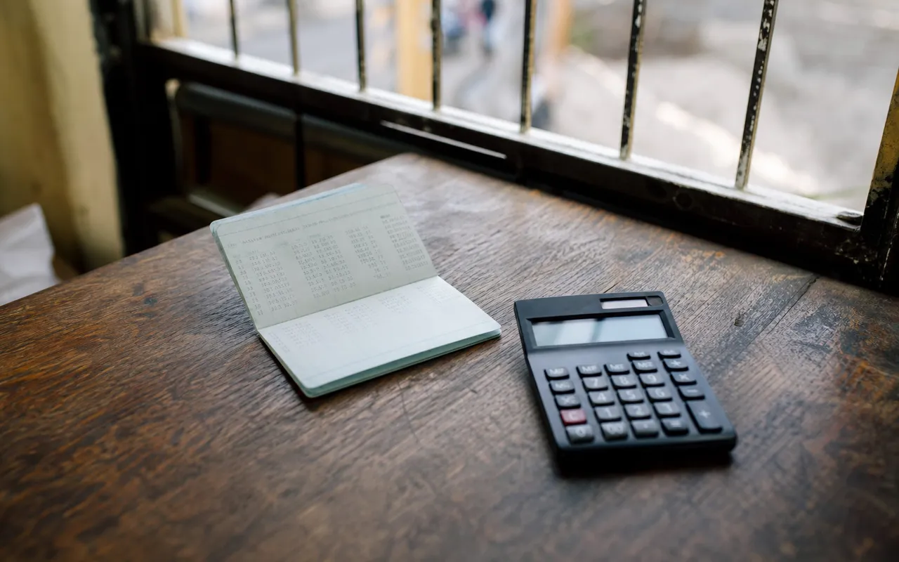 Carnet d'épargne et calculatrice posés sur une table en bois, lumière naturelle douce