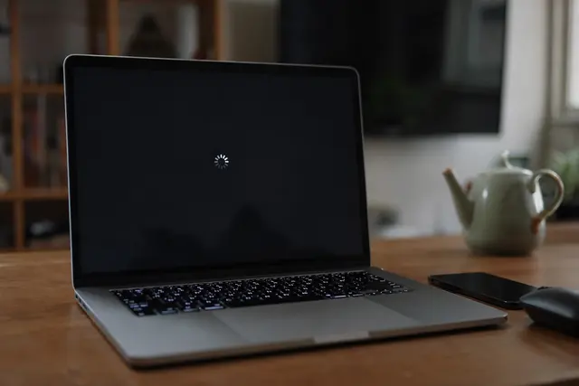 Ordinateur portable ouvert sur un bureau, écran noir au moment d'un redémarrage, lumière tamisée