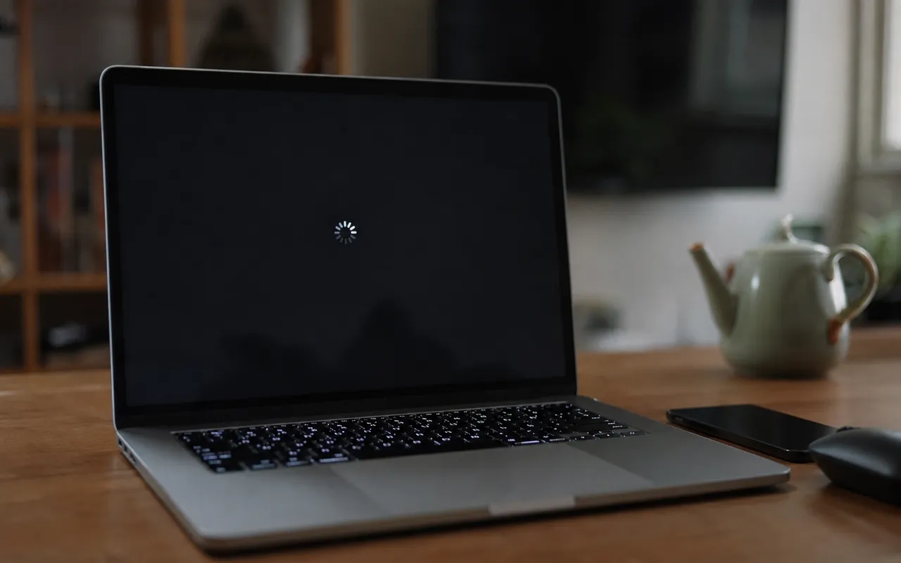 Ordinateur portable ouvert sur un bureau, écran noir au moment d'un redémarrage, lumière tamisée