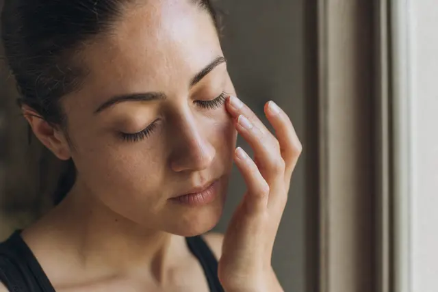 Personne se frottant délicatement le contour de l'œil, lumière douce, ambiance calme et intimiste