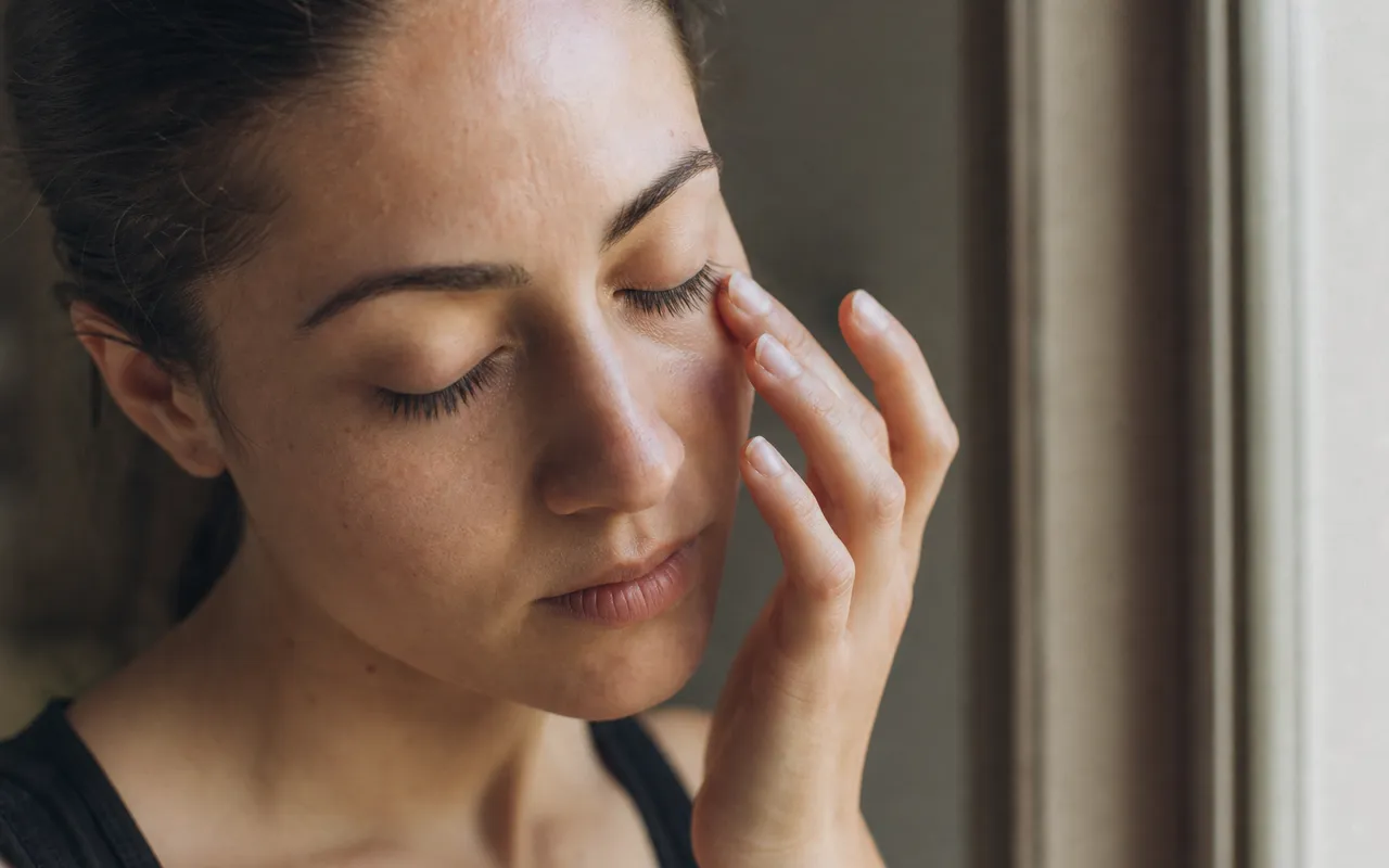 Personne se frottant délicatement le contour de l'œil, lumière douce, ambiance calme et intimiste