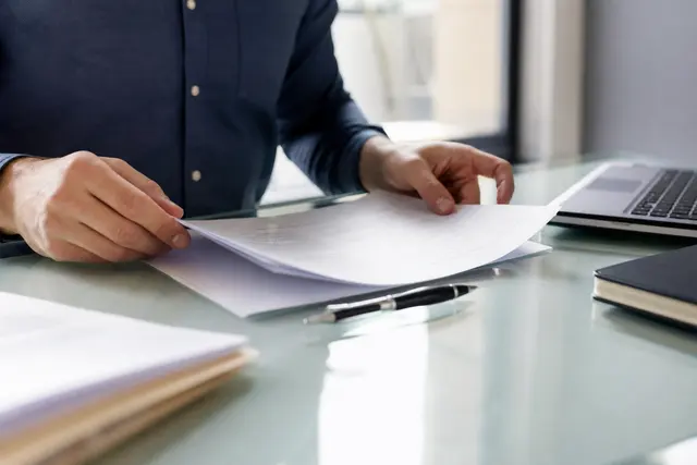 Bureau clair avec un contrat de travail posé sur la table, stylo à côté, mains d'une personne en train de le consulter