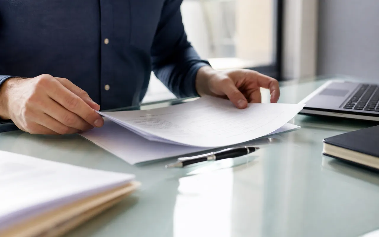 Bureau clair avec un contrat de travail posé sur la table, stylo à côté, mains d'une personne en train de le consulter