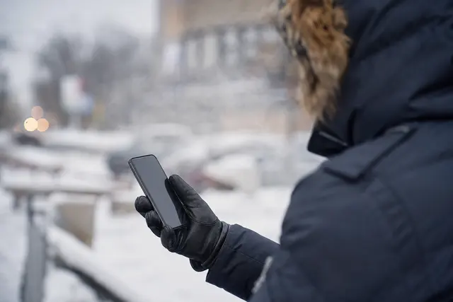 Main tenant un smartphone à l'extérieur en hiver, avec de la buée et un environnement froid en arrière-plan