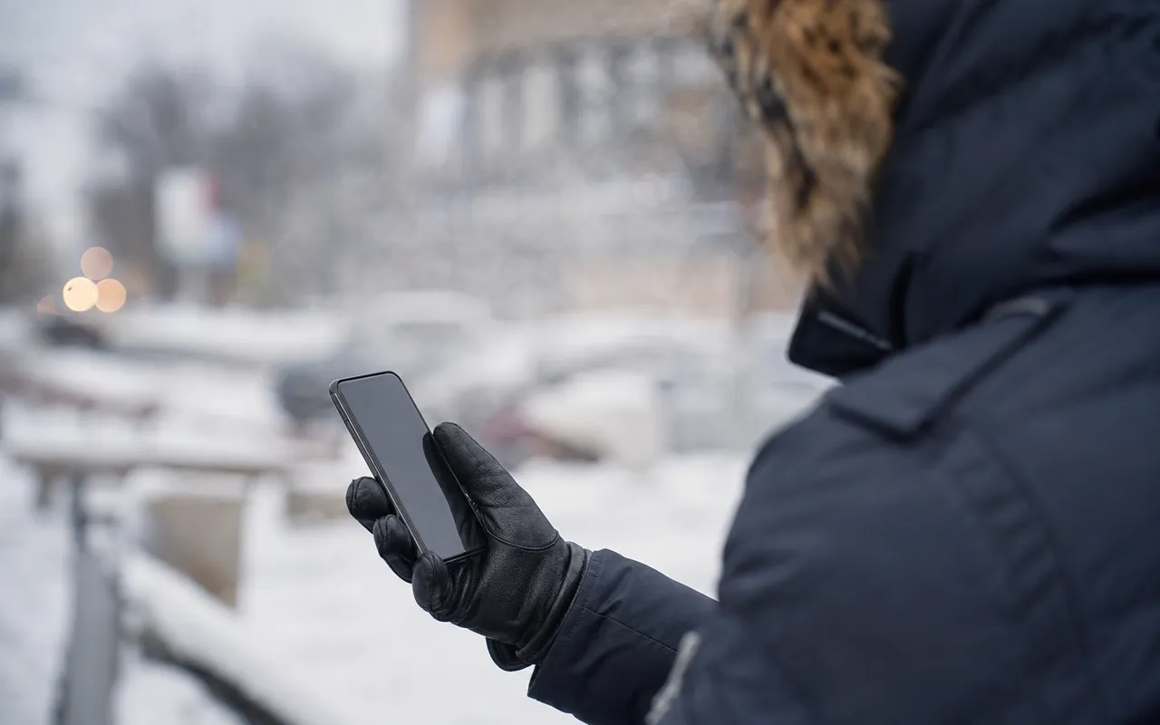 Main tenant un smartphone à l'extérieur en hiver, avec de la buée et un environnement froid en arrière-plan