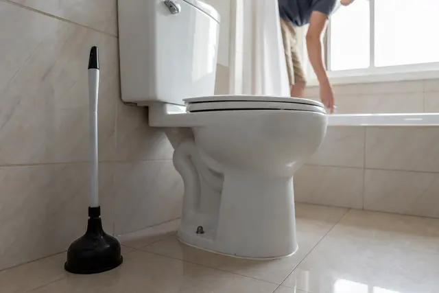 Cuvette de toilettes vue de profil avec une ventouse posée à côté, ambiance salle de bain lumineuse