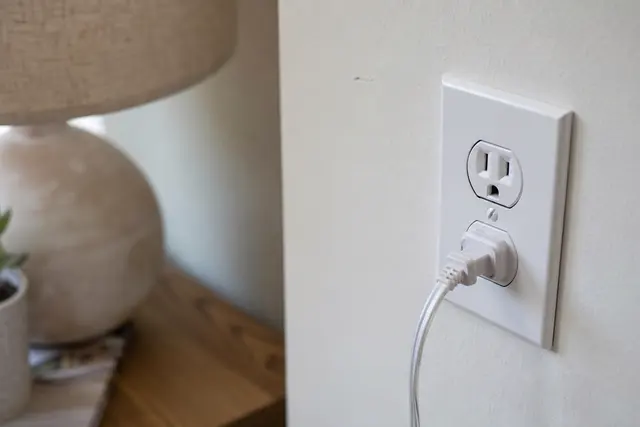 Gros plan sur une prise électrique murale blanche avec une lampe branchée, intérieur domestique en lumière naturelle