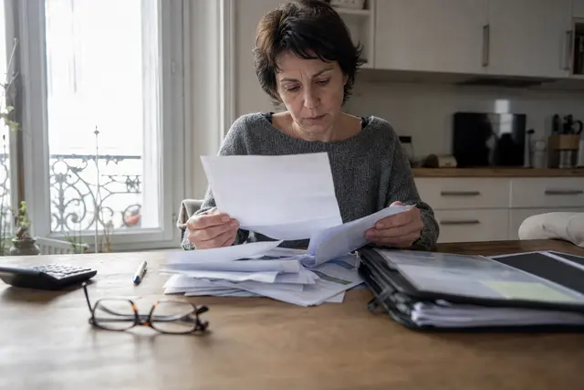 Personne assise à sa table de cuisine examinant une lettre de relance et des relevés bancaires étalés devant elle
