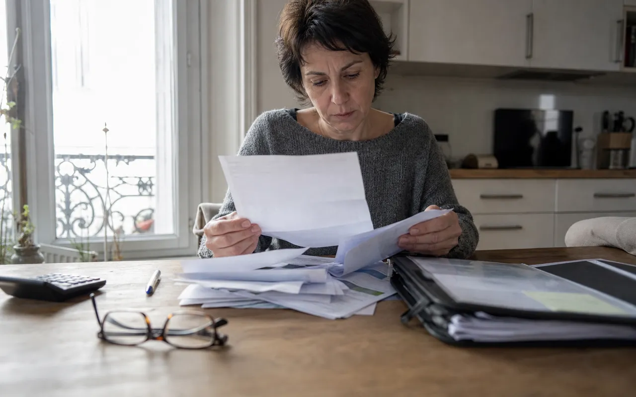 Personne assise à sa table de cuisine examinant une lettre de relance et des relevés bancaires étalés devant elle