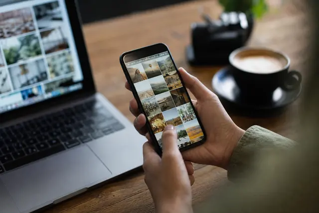 Personne tenant un smartphone et faisant défiler une galerie de photos, écran allumé dans une lumière douce d'intérieur