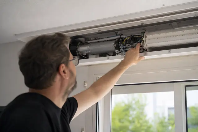 Personne examinant le coffre d'un volet roulant électrique bloqué depuis l'intérieur d'une maison